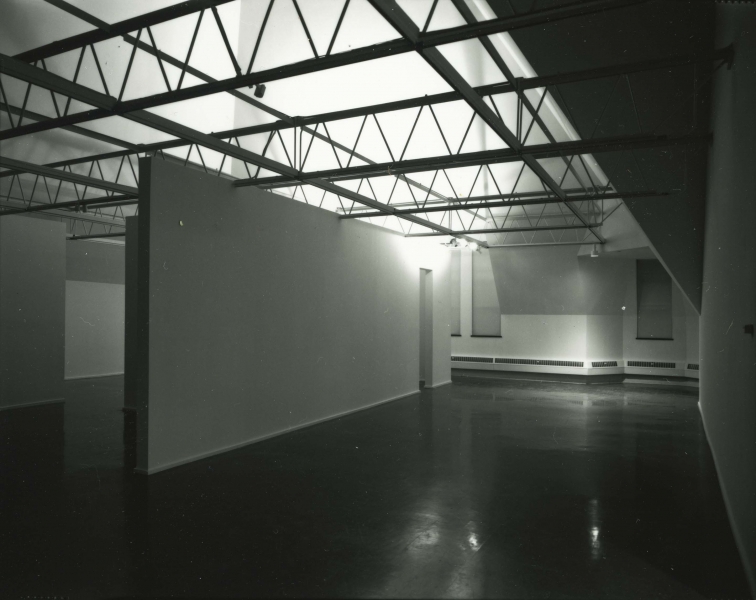 A large cube stands in the gallery, projecting a video of a calm face being covered in a dark liquid.