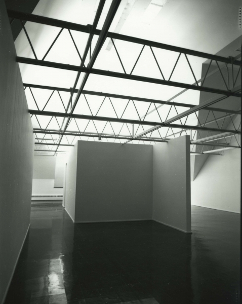 A large cube stands in the gallery, projecting a video of a calm face being covered in a dark liquid.