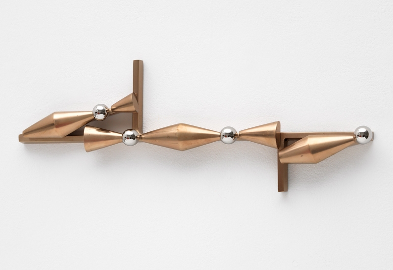 A stand of yellow cherrywood mounted on a wall with a small white, red and aluminum sculpture on top of it