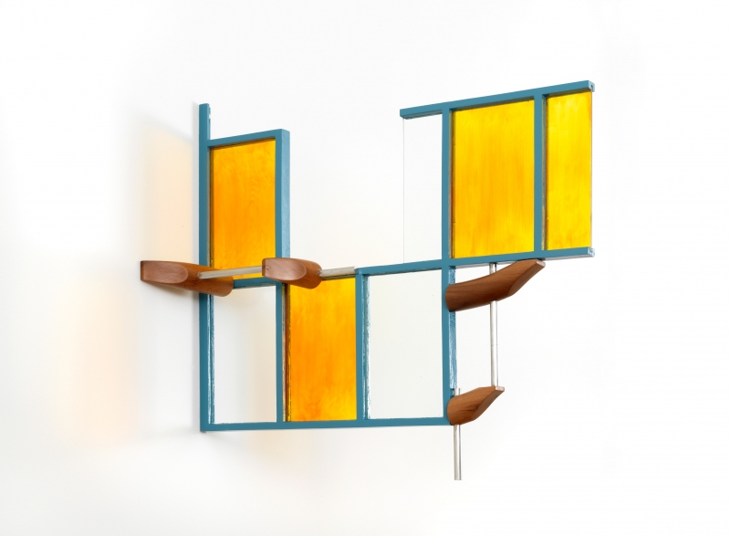 A stand of yellow cherrywood mounted on a wall with a small white, red and aluminum sculpture on top of it