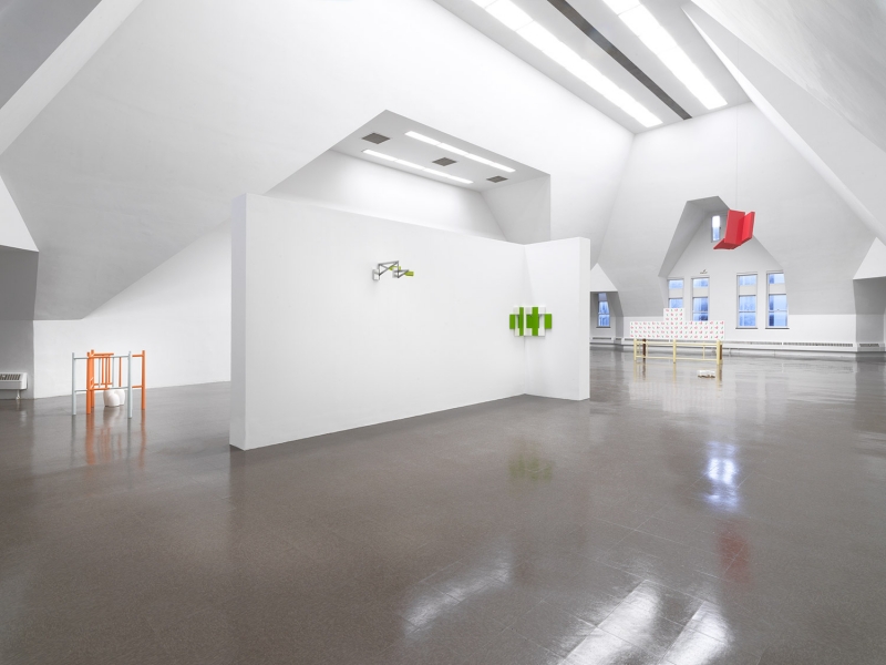 A stand of yellow cherrywood mounted on a wall with a small white, red and aluminum sculpture on top of it