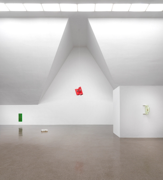 A stand of yellow cherrywood mounted on a wall with a small white, red and aluminum sculpture on top of it