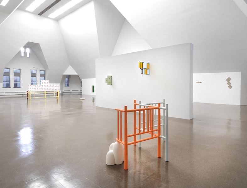 A stand of yellow cherrywood mounted on a wall with a small white, red and aluminum sculpture on top of it