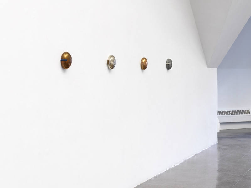 A stand of yellow cherrywood mounted on a wall with a small white, red and aluminum sculpture on top of it