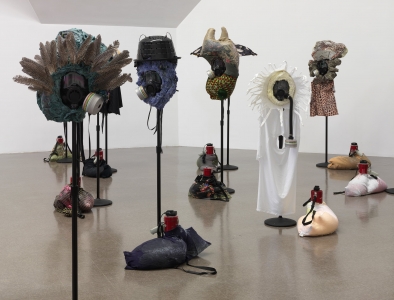 Mixed-media sculptures cover gas masks perched on poles, bags with a megaphone resting at the base of each pole.