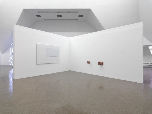 A plain canvas, a section of gray fading to white, mounted near two small bronze sculptures on walls at ninety-degree angles
