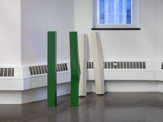 Four metal poles: two green ones stand near the wall, two white lines lean against it