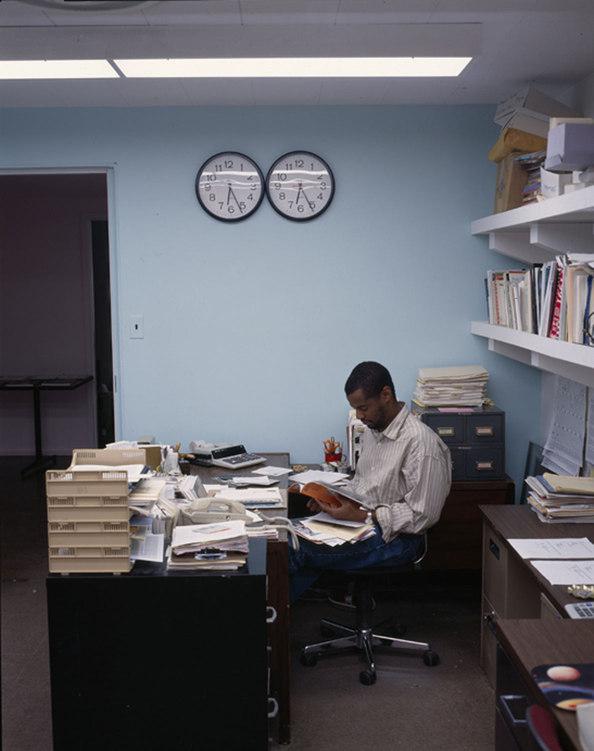 Hamza Walker works at a desk covered in papers.