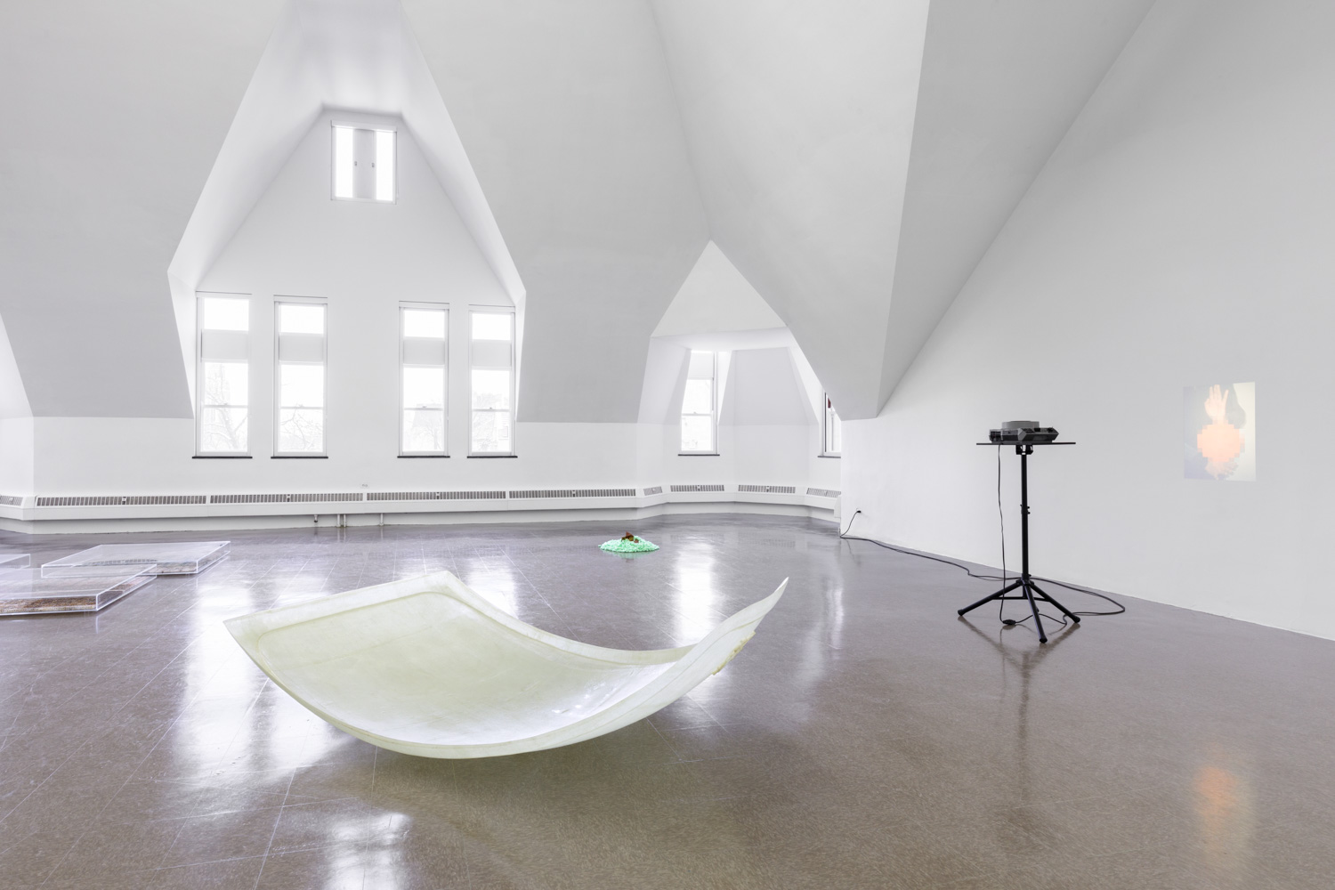 A curved fiberglass sheet rests on the floor near a projector playing a movie on a wall.