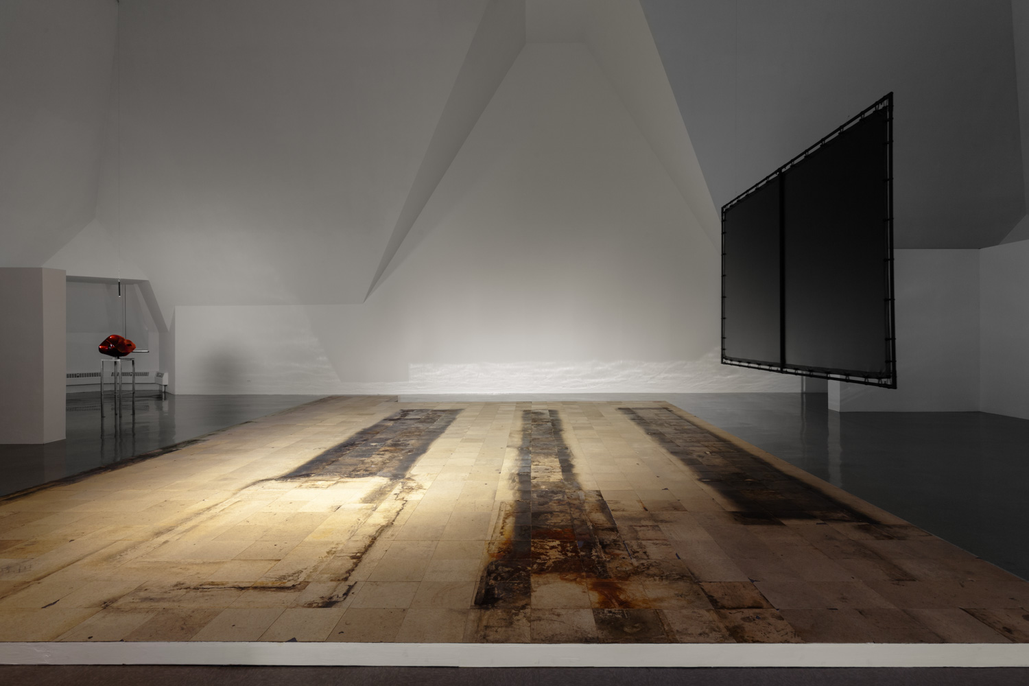 A stained, scuffed, cracked vinyl platform stretches across the room, a movie screen hanging from the ceiling at right.