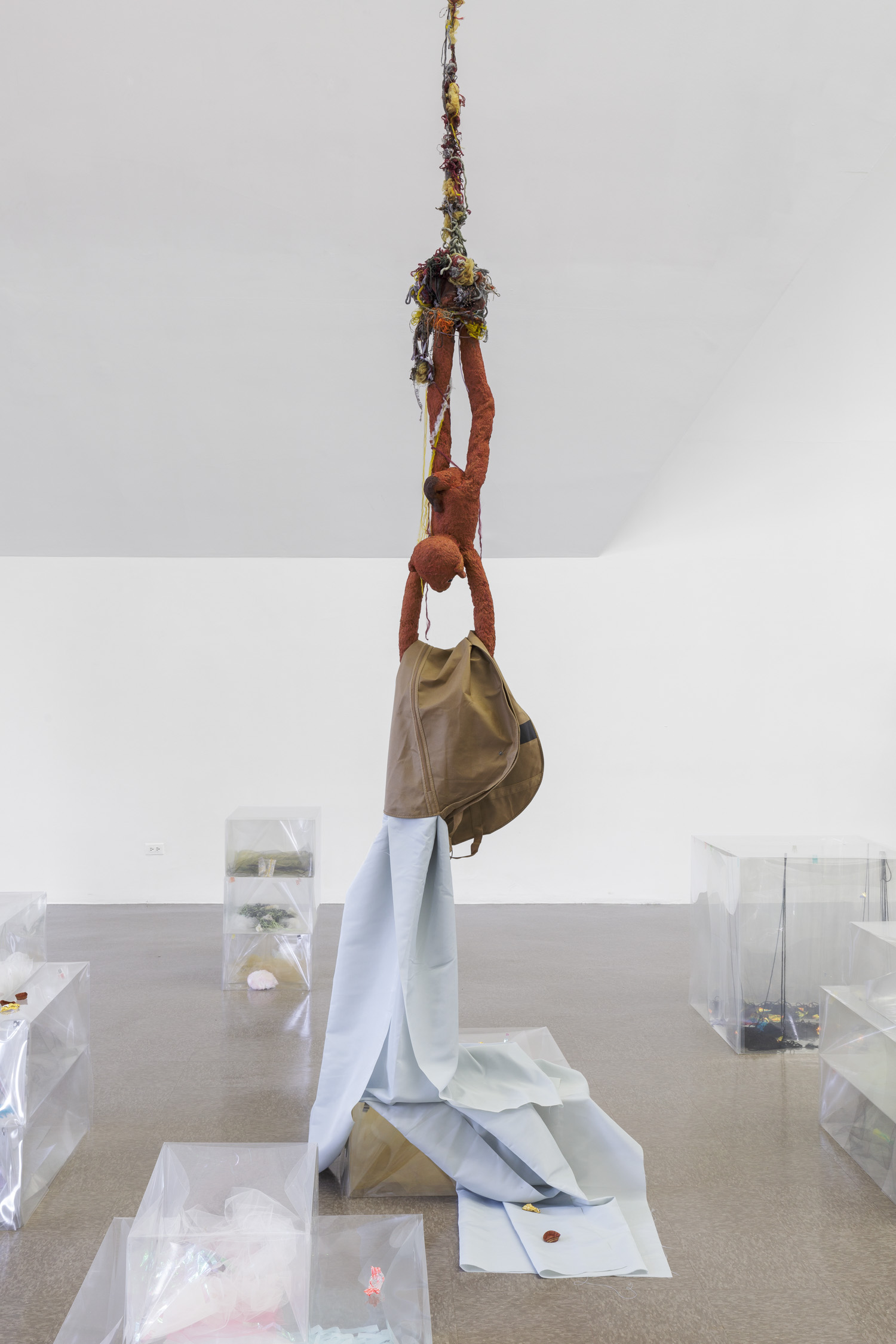 Siena rubber figure, legs dangling from a line of yarn suspended at the ceiling, holds cloth in its arms