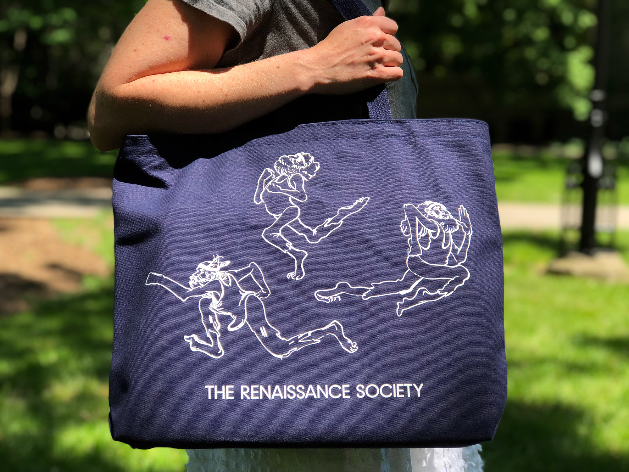 A person holds a dark blue tote bag with white print.