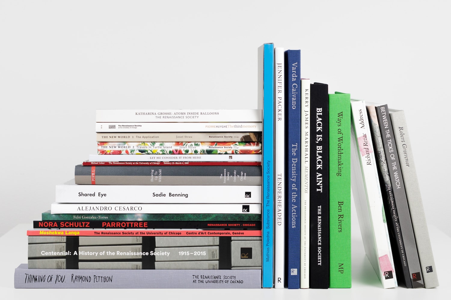 Fourteen books, stacked horizontally, sit next to ten books placed vertically against the stack.